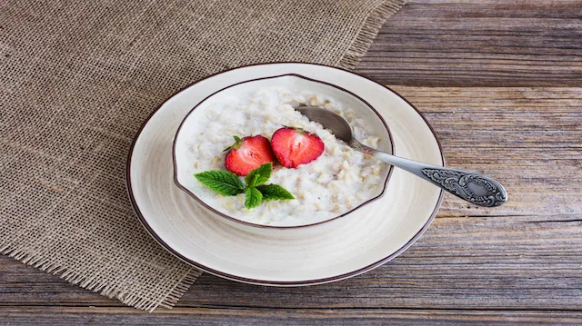 Oatmeal porridge in bowl topped with fresh strawberries on old wooden table