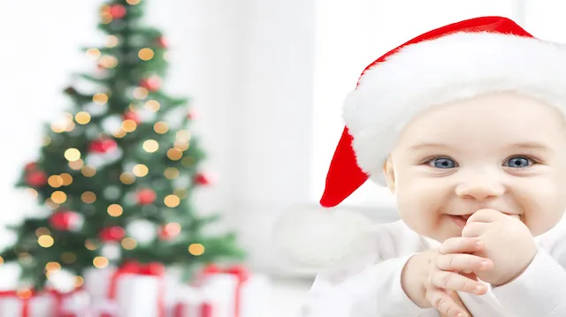 happy baby in santa hat over christmas tree lights