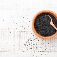 Black sesame seeds in a bamboo bowl on white wooden background. Top view.