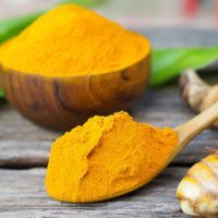 Turmeric powder and fresh turmeric in wooden spoon with green leaf on old wooden table. Herbal