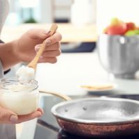 Woman putting coconut oil on frying pan in kitchen, closeup